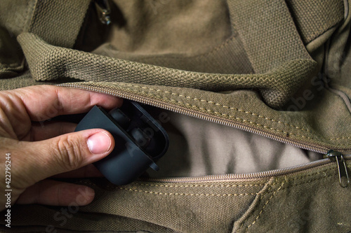 Hand takes off a case of wireless headphones from a suitcase pocket.