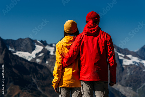 People in colorful jackets on the background of the mountains, rear view. An active couple is engaged in Hiking. A young couple is engaged in tracking. Hiking. People in the mountains