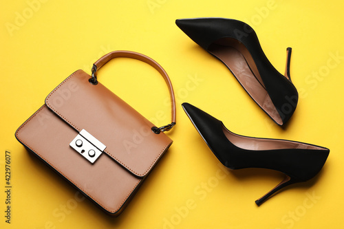 Pair of elegant high heel shoes and handbag on yellow background, flat lay