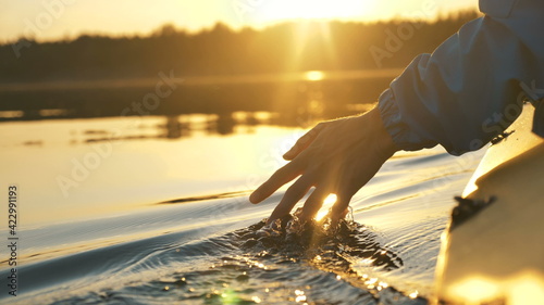 man puts fingers down in lake kayaking against backdrop of golden sunset, unity harmony nature