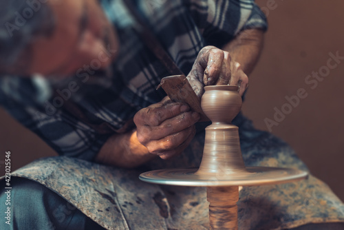 A male artisan in a pottery workshop makes a piece of clay behind a pottery wheel. Traditional pottery craft.