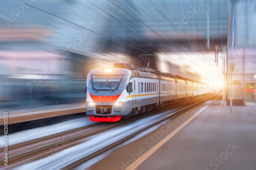 Speed suburban train with motion blur rides city station.