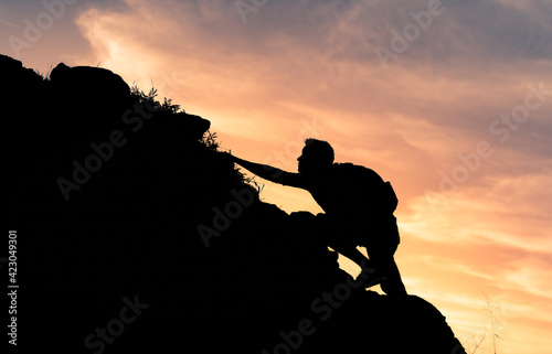 Young man climbing up steep edge of mountain 