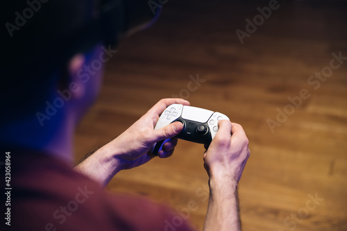 Closeup of man's hands playing video games on gaming console in front of TV widescreen. Man play with Play station 5 Dual Sense controller. Colorful lights.