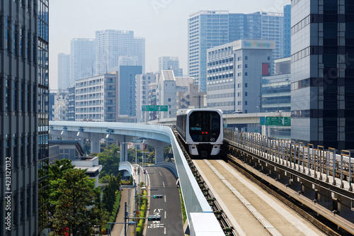 Scenic view of a train traveling on elevated rails of Yurikamome Line in Downtown Tokyo, with a background of modern buildings near Takeshiba Station under blue sunny sky ~ Scenery of a vibrant city