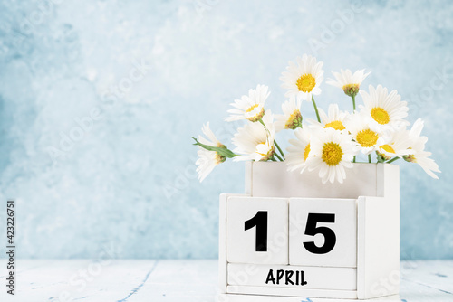 cube calendar for april decorated with daisy flowers over blue with copy space