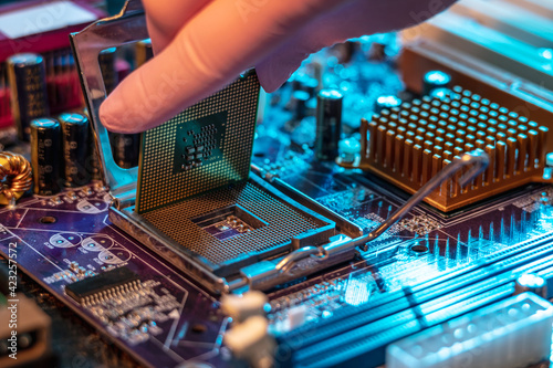 Engineer's gloved hand is holding the CPU chip on the background of the motherboard. High-tech hardware microelectronics