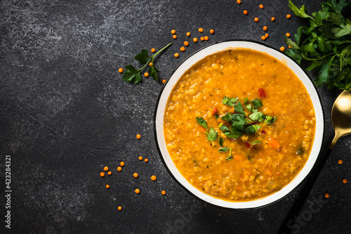 Lentil soup with vegetables on black stone table.