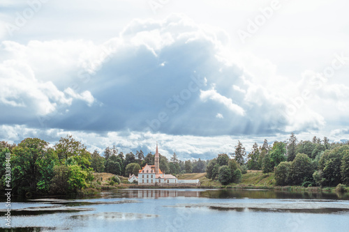 Gatchina, Saint-Petersburg, Russia, 25 August 2020: Priory palace by the Black lake in summer on background of epic cloudy sky. The sun's rays shine through the clouds on the historic building.