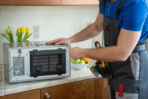 Young repairman fixing and repairing microwave oven by screwdriver in kitchen