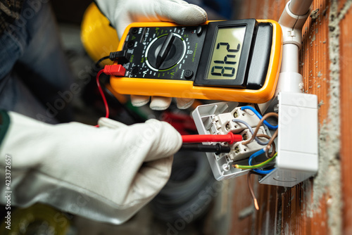 View from above. Electrician worker at work with the tester measures the voltage in a switch of a residential electrical system. Working safely with protective gloves. Construction industry.