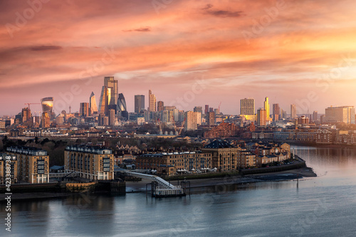 The urban skyline of London, United Kingdom, along the Thames river to the City during a colorful sunrise with orange and pink cloudscape 