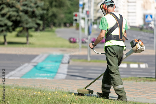 Road landscaper man worker cutting grass along city street