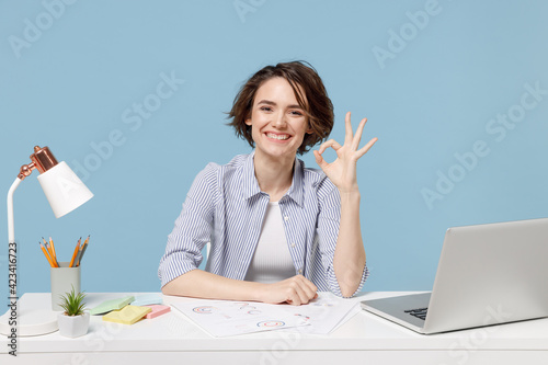 Young successful employee business woman in casual shirt sit work at white office desk with pc laptop show okay gesture isolated on pastel blue background studio portrait Achievement career concept