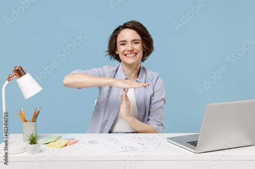 Young happy successful employee business woman in casual shirt sit work at white office desk with pc laptop hold stop gesture hands perpendicularly isolated on pastel blue background studio portrait