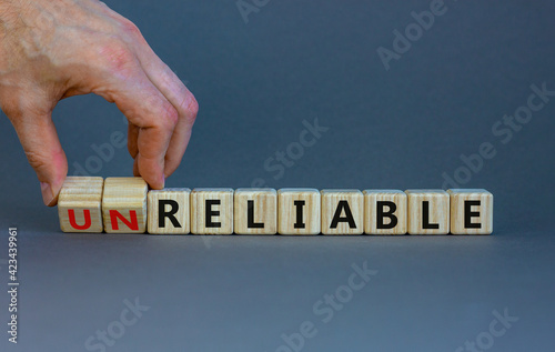 Unreliable or reliable symbol. Businessman turns wooden cubes and changes the word unreliable to reliable. Beautiful grey background, copy space. Business and unreliable or reliable concept.