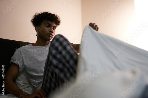 Relaxation. Young guy wearing pajamas going to bed, covering himself with a duvet in the bedroom