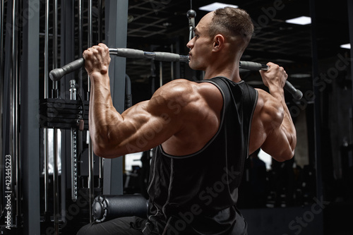 Muscular man workout in gym, doing exercise for back, lat pulldown. Strong male rear view