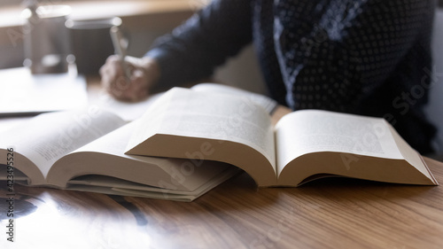 Close up woman student writing notes from textbook, sitting at desk with books, young female preparing for university or college exams, doing homework, school assignments at home, education concept