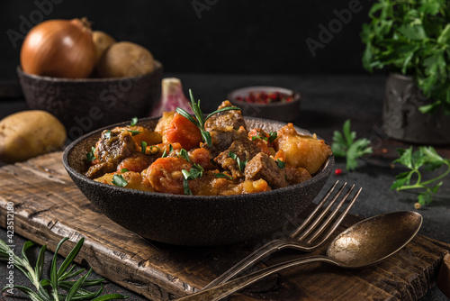 Irish stew made with beef, potatoes, carrots and herbs in a plate with cutlery on black background