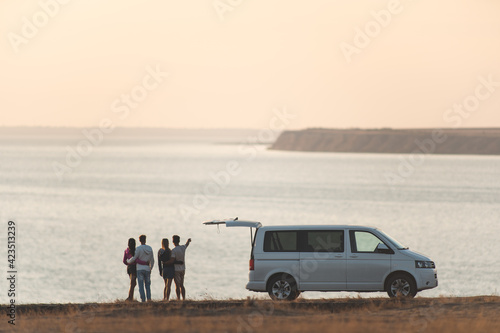 The four friends standing near the minivan against the sunset sky