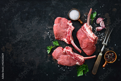 Raw veal Frenched Racks meat with ingredients on rustic dark background