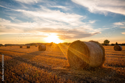 Beautiful bright sun rays under horizon over the field after harvesting. Straw bales outdoors on warm sunny summer evening.