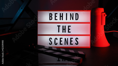 Behind the scenes light box. Text on cinema light box. Megaphone and director chair and movie slate beside. Background LED color. Camera in video production studio. Behind the scene concept.