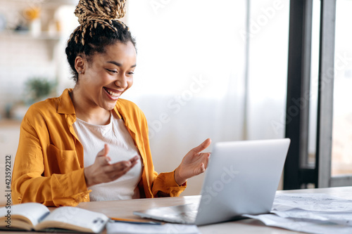 Online communication. Confident joyful beautiful african american young female student or freelancer with afro dreadlocks, study remotely, talks by online conference with coworkers or teacher, smile