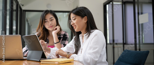 Horizontal photo of two female college student working on digital tablet and talking about lessons comparing together.