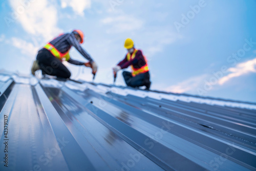 Selective focus roof, construction worker safety wear using electric drill tools install on new roof metal sheet, Roof construction concept.