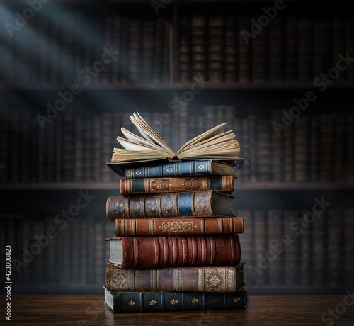 A stack of old books on table against background of bookshelf in library. Ancient books as a symbol of knowledge, history, memory. Conceptual background on education, literature topics.
