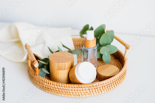 Natural cosmetics set in eco-friendly packaging in rattan tray with eucalyptus and towel. SPA, bath beauty products.