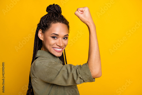 Photo portrait of african american girl flexing biceps isolated on vivid yellow colored background