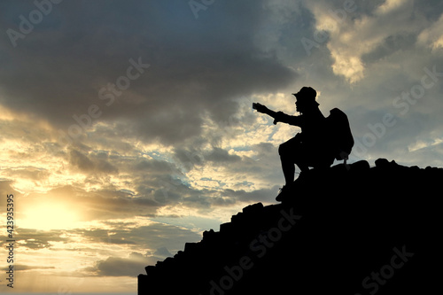 Silhouette of young male tourists Sit back and see the sunset and take pictures at the top of the mountain with your backpack.