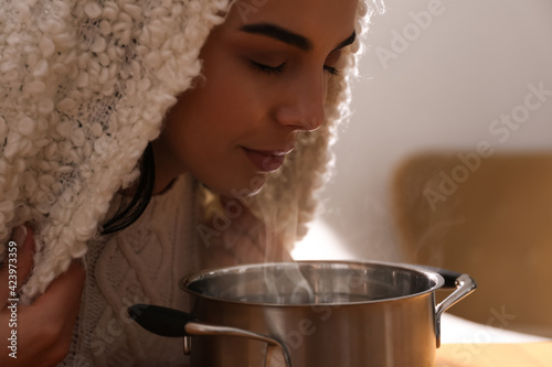 Woman with plaid doing inhalation above saucepot indoors
