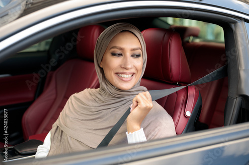 Smiling Muslim Woman In Hijab Putting On Seat Belt