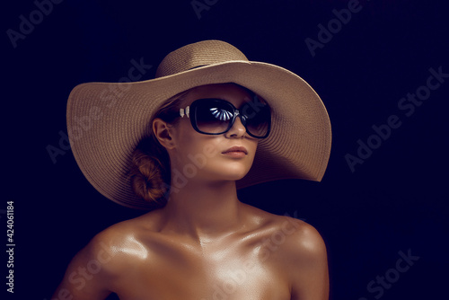 Beauty photo of attractive woman wearing straw hat and big sunglasses posing on dark studio background