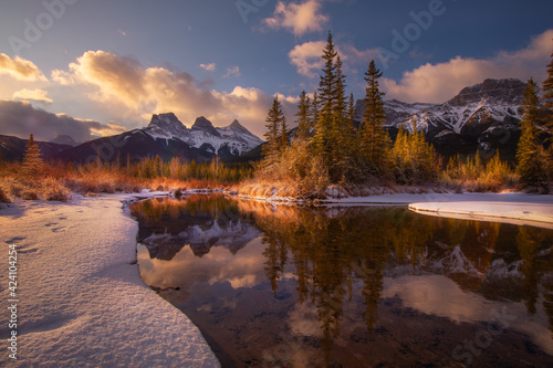 Three Sisters from Policeman Creek after sunrise reflected in the Bow River, Canmore, Alberta, Canada