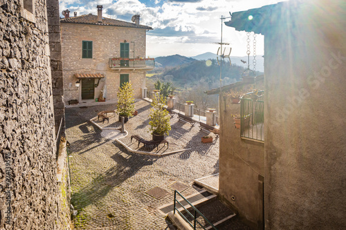 The small medieval village of Capranica Prenestina in Lazio, province of Rome. A small square, with a cobblestone floor, with benches and a fountain, overlooks the mountain panorama.