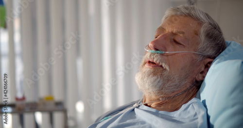 Close up portrait of senior man with nasal breathing tube lying in hospital bed