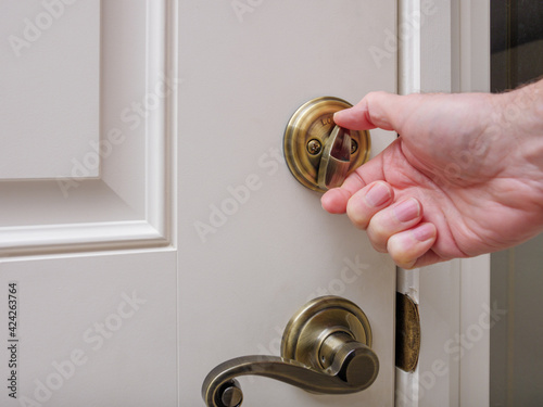 Close up of man locking deadbolt door lock on white entry door. Home security burglar and robbery prevention.