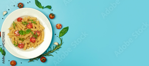 Food pasta on a blue background. Italian fusilli pasta with tomatoes, herbs and basil on a white plate. Healthy food concept.