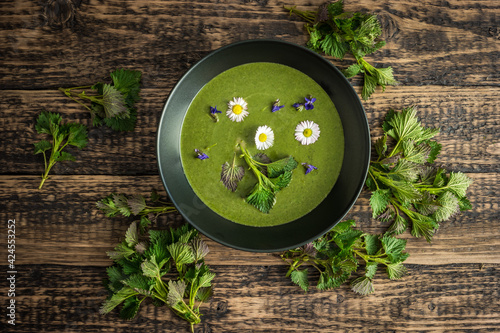 Healthy green spring nettle soup with edible flowers garnished with nettle leaves served on Green Thursday