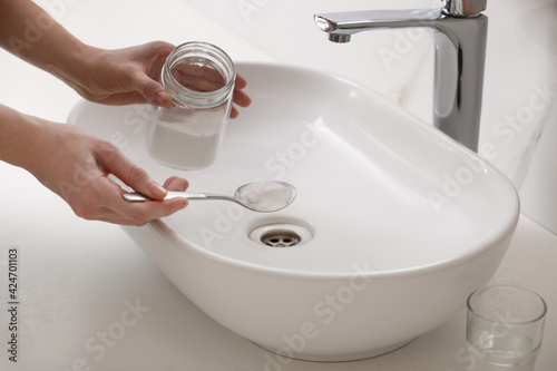 Woman using baking soda to unclog sink drain in bathroom, closeup