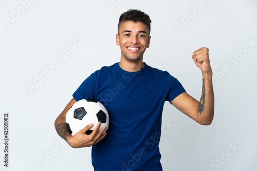 Young Brazilian man over isolated background with soccer ball celebrating a victory