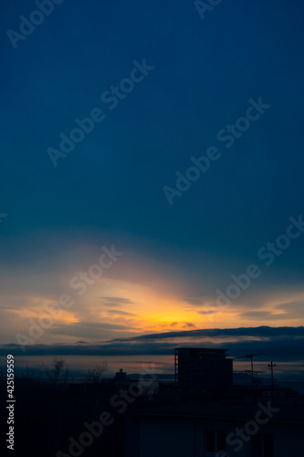 view on atmospheric sunset in blue, yellow and orange tones over sea and dark silhouettes of residential buildings. vertical travel content. selective focus