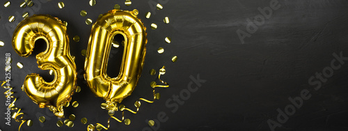 gold foil balloon number thirty. Birthday or anniversary greeting card with the inscription 30. Black concrete background. Anniversary celebration. Banner.