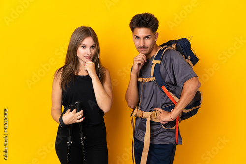 Young mountaineer couple with a big backpack isolated on yellow background smiling and looking to the front with confident face