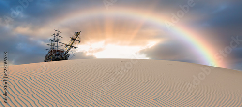 Silhouette of old ship on desert with rainbow at amazing sunset 